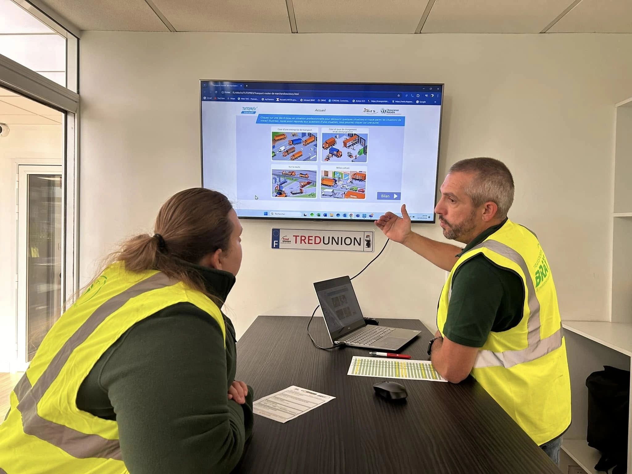 Deux personnes en train de discuter devant une télé projetant des consignes de sécurité